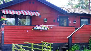 A red wooden building with a red and white striped awning, a flower box on the front, and a wooden fence in front.