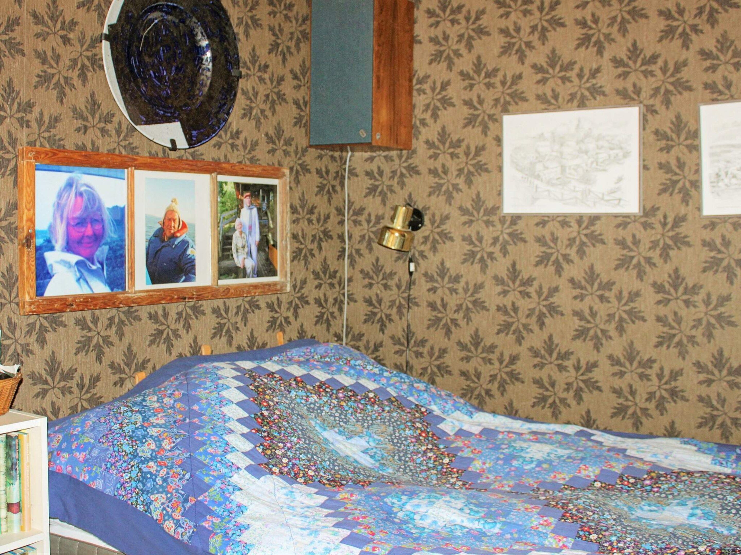 A room with a bed, a wall clock, framed photos, and a patterned wallpaper.