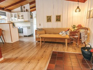A cozy living room with a sofa, a wooden coffee table, and a wicker chair. There is a kitchen area with white cabinets and a stove. - 4 Star Holiday Home in Hadsund (Hadsund)