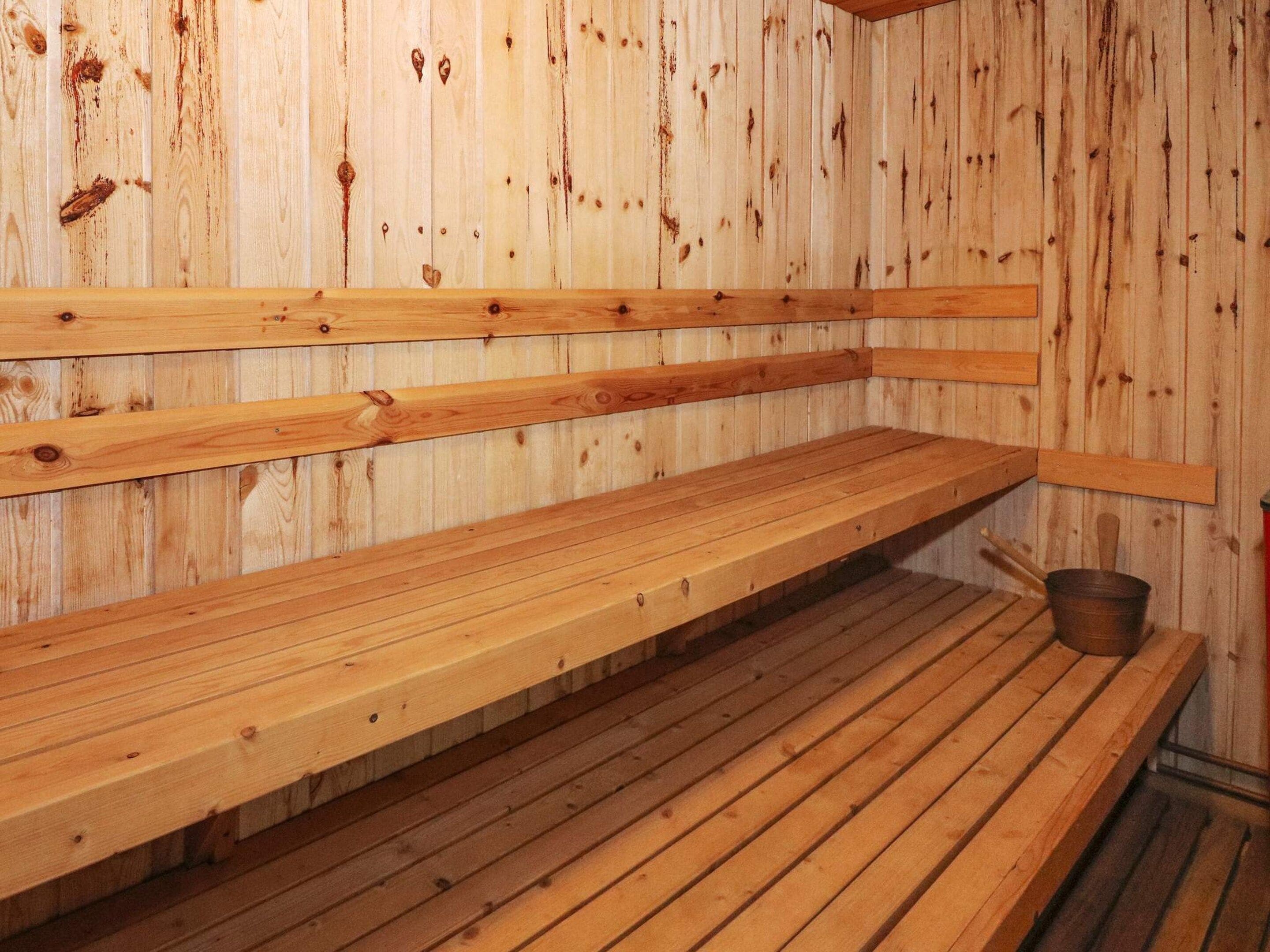 A sauna with wooden benches and a metal bucket.