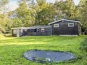A two-story house with a small attached garage, a trampoline in the yard, and a wooded area in the background.