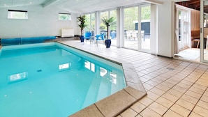 En indendørs swimmingpool med klart, blåt vand, flisegulv og udsigt til terrassen.