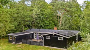 Et moderne hus med stor terrasse, solpaneler og omgivet af tæt bevoksning.