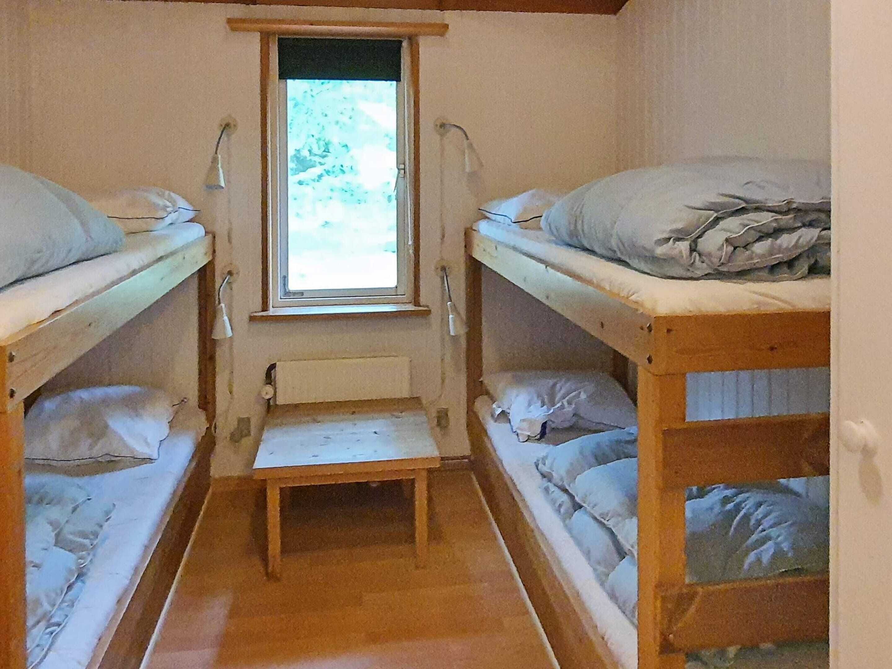A narrow room with bunk beds, a small table, and a window.