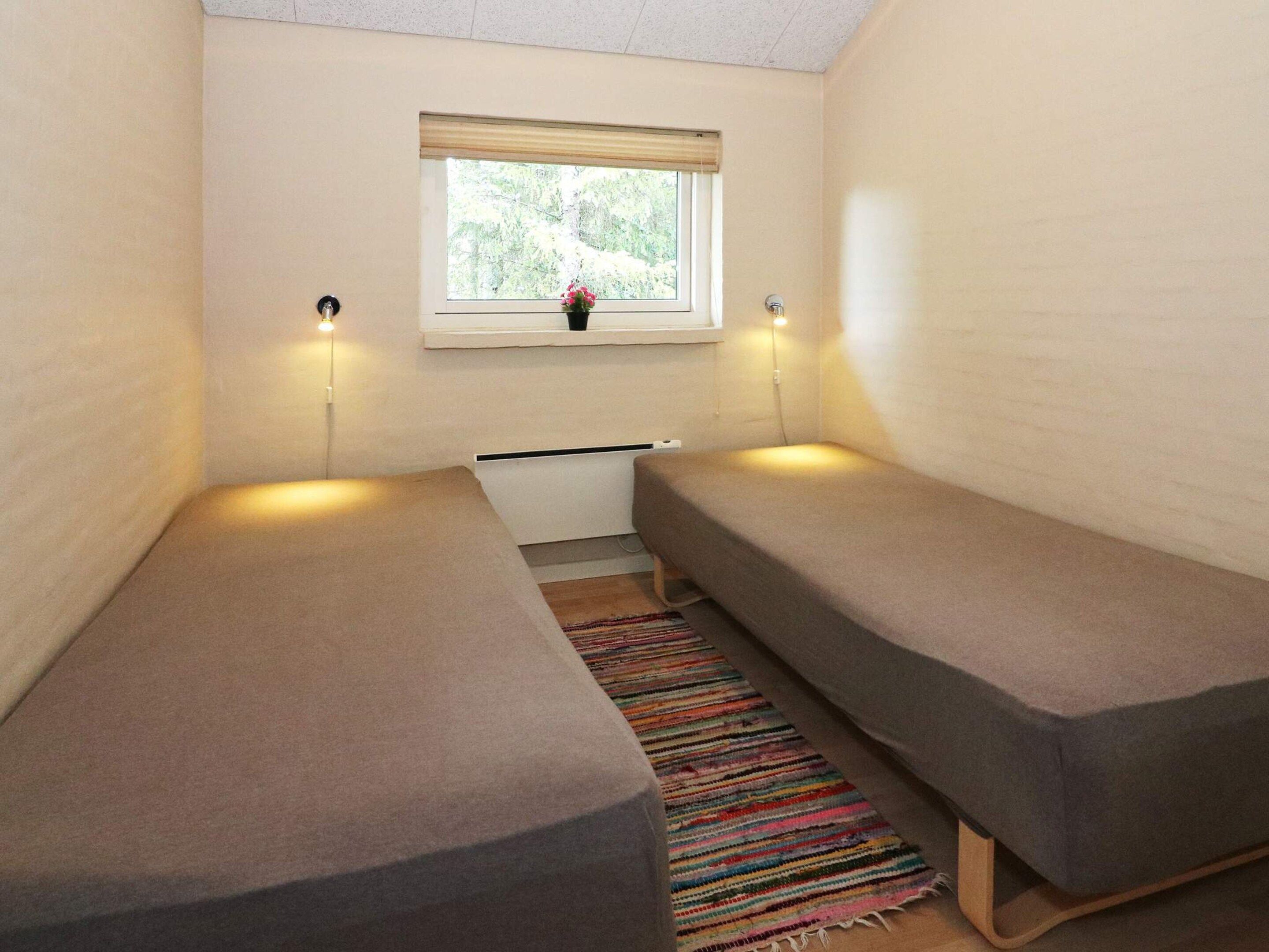 A small, single-room accommodation with two single beds, a window with a view of greenery, and a small table with a power outlet.