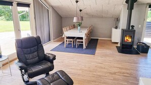 Uma sala de estar acolhedora com um sofá de couro preto, uma mesa de jantar com cadeiras, uma lareira e uma janela grande com cortinas.