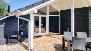 Um pátio externo com deck de madeira, portas de correr de vidro e móveis de vime.