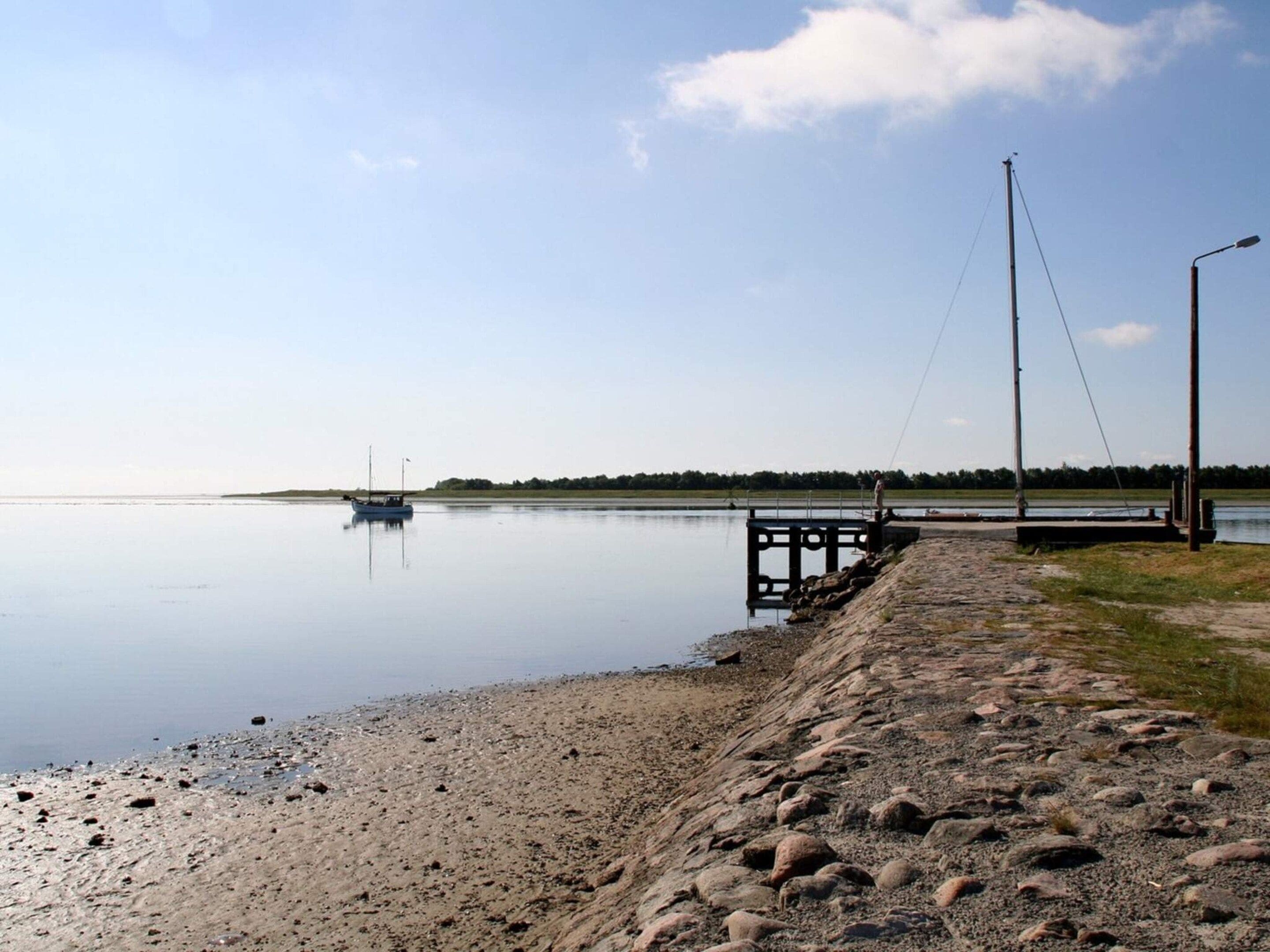 A calm lake with a dock and a boat, surrounded by a rocky shoreline and a clear sky.