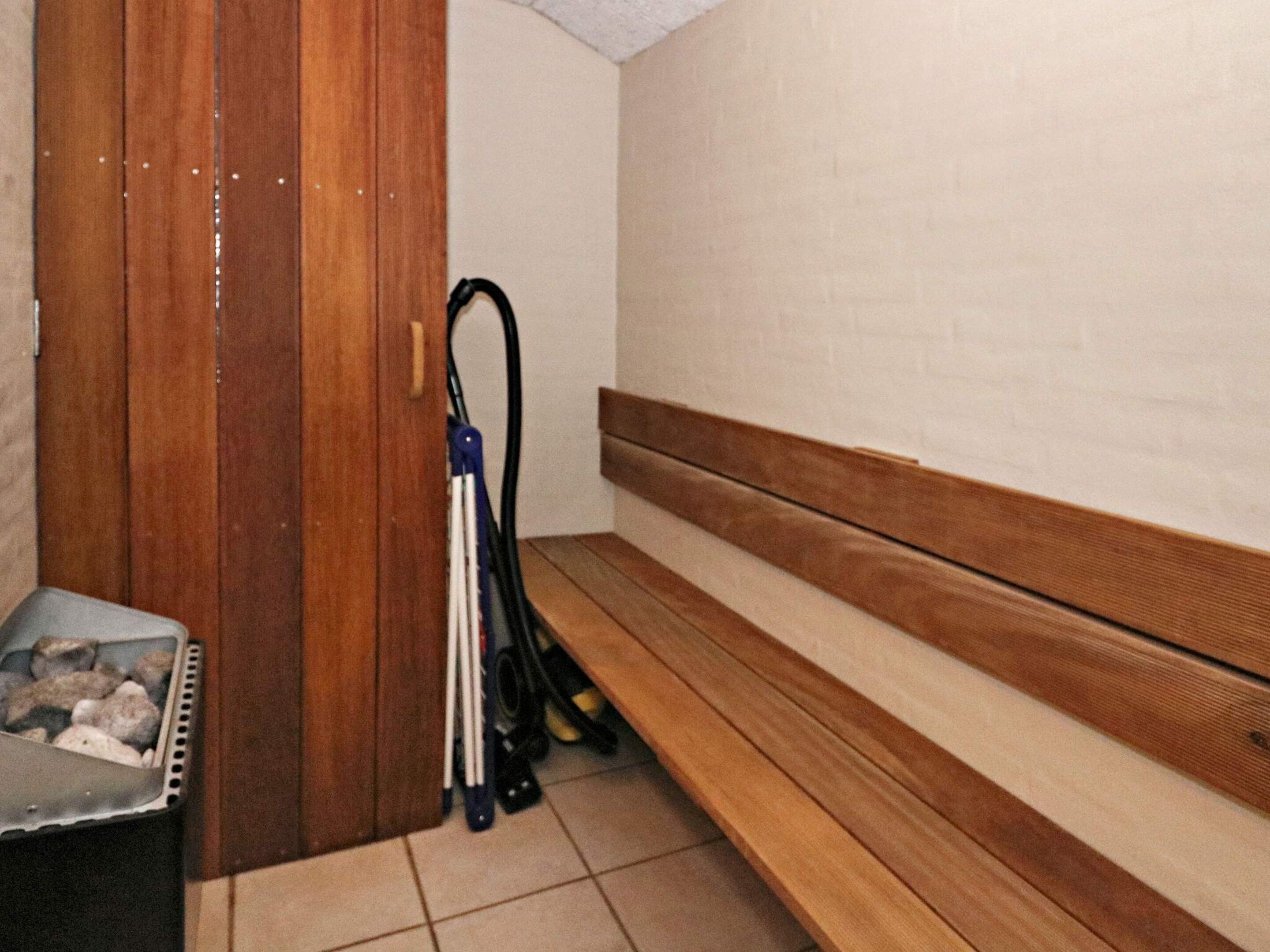 A sauna room with a wooden bench, a heater, and a metal container with rocks.