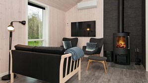 A modern living room with a black sofa, a wooden chair, a TV mounted on the wall, and a wood-burning stove. - Modern Retreat by Skovmose-by Traum (Sydals)