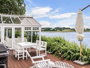 A conservatory with a view of a lake, outdoor seating, and a grill. - 5 Star Holiday Home in Hejls (Hejls)