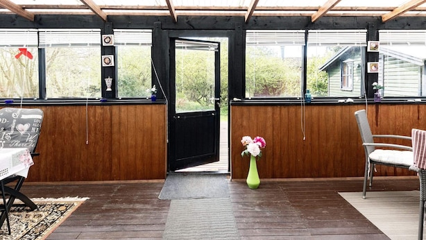An open wooden door leading to a covered outdoor area with a bench and a chair, a vase with flowers, and a view of greenery outside. - 5 Person Holiday Home in Gedser (Gedser)