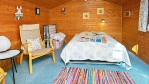 A cozy wooden cabin bedroom with a bed, a chair, a small table, and a colorful rug. - 5 Person Holiday Home in Gedser (Gedser)