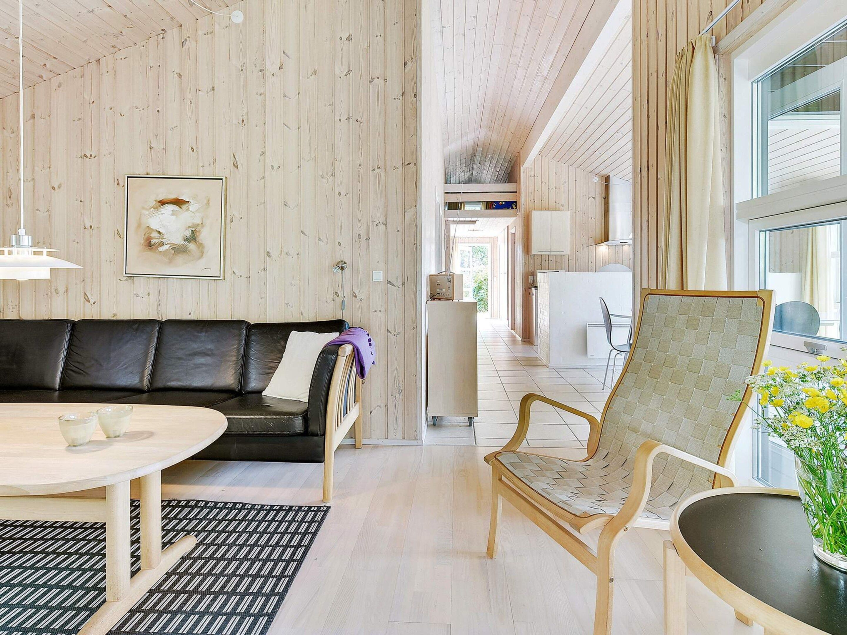 Un intérieur moderne avec un plafond en bois, un canapé en cuir noir, une chaise en bois, une petite table et une fenêtre donnant sur un beau paysage.