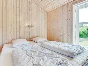 A bedroom with a wooden slat ceiling, a bed with white bedding, and a window with a view of greenery. - 4 Star Holiday Home in Albaek (Aalbaek)