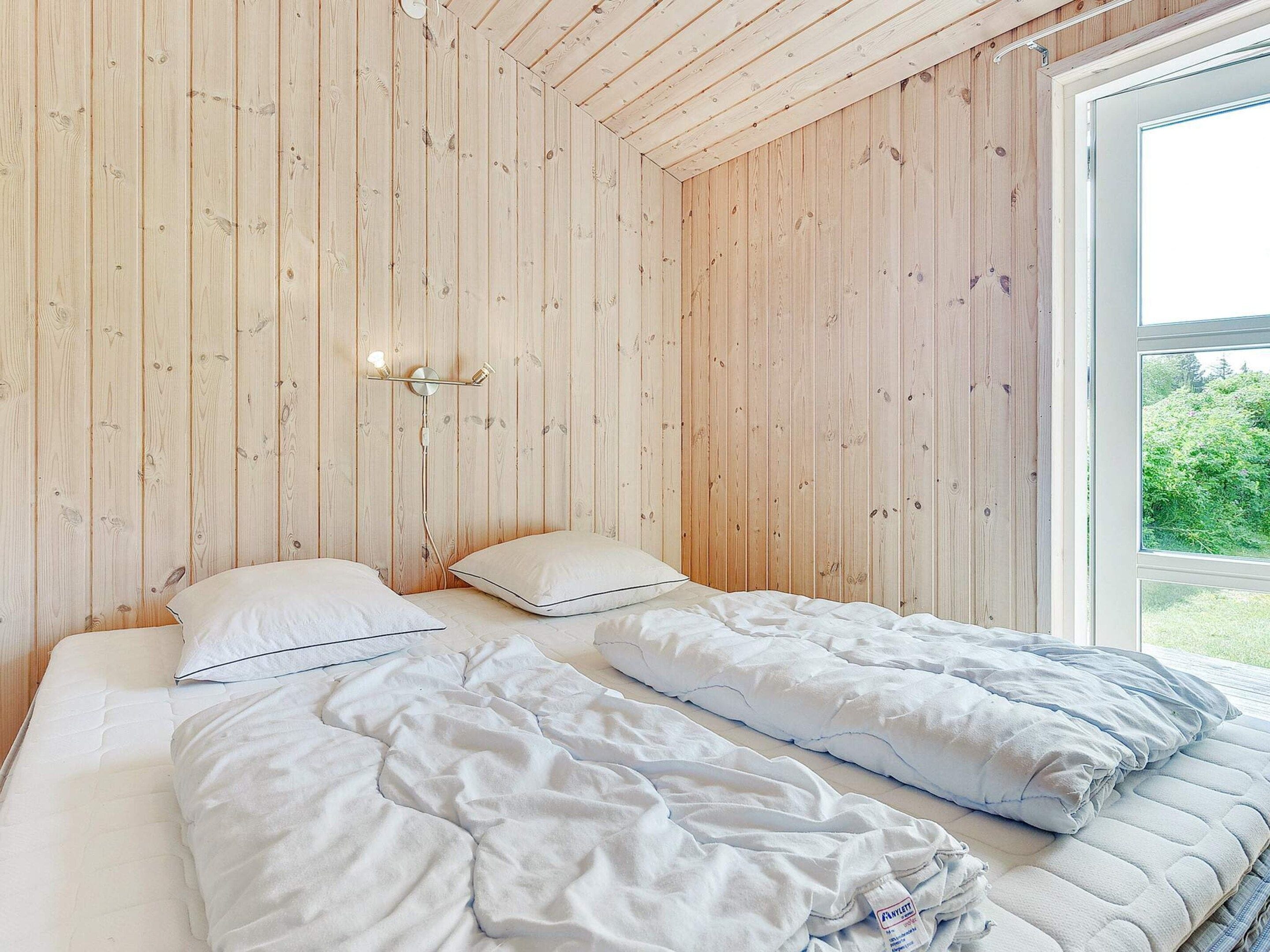 A bedroom with wooden panel walls, a bed with white bedding, and a window with a view of greenery.