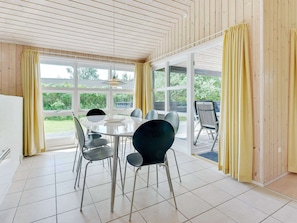 A dining area with a round table, chairs, and large windows with curtains.
