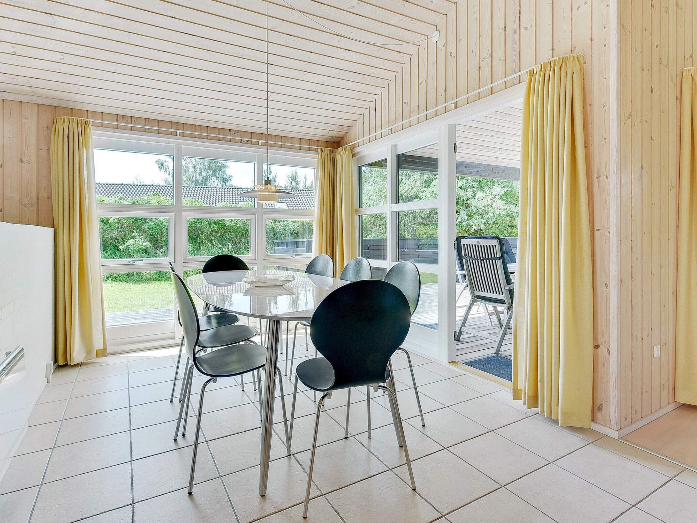 A dining area with a round table and chairs, large windows, and a view of greenery outside.