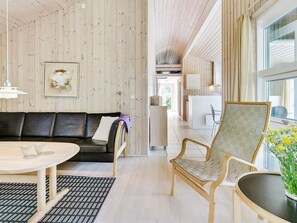 A modern interior with a wooden wall, a black leather sofa, a wooden chair, a small table, and a view through a window. - 8 Person Holiday Home in Albaek (Aalbaek)
