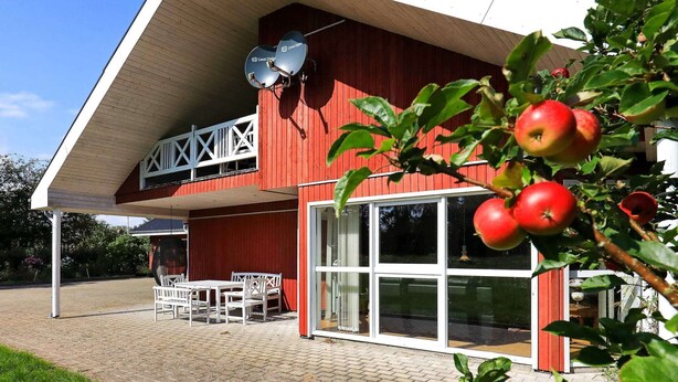 Ein rotes Gebäude mit überdachter Terrasse, Satellitenschüsseln und einem Apfelbaum.