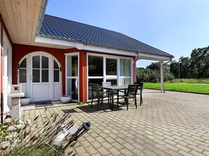 A house with a red exterior, a tiled roof, and a paved patio with a table and chairs.