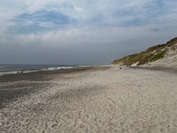 Una playa de piedras y arena, un acantilado cubierto de hierba y el océano.