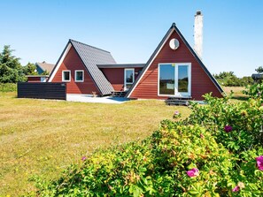 Una casa moderna con techo inclinado, chimenea y un ventanal grande.