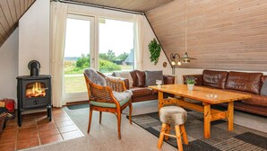 A cozy living room with a wood-burning stove, leather sofa, and a dining table. - 6 Person Holiday Home in Hvide Sande (Hvide Sande)