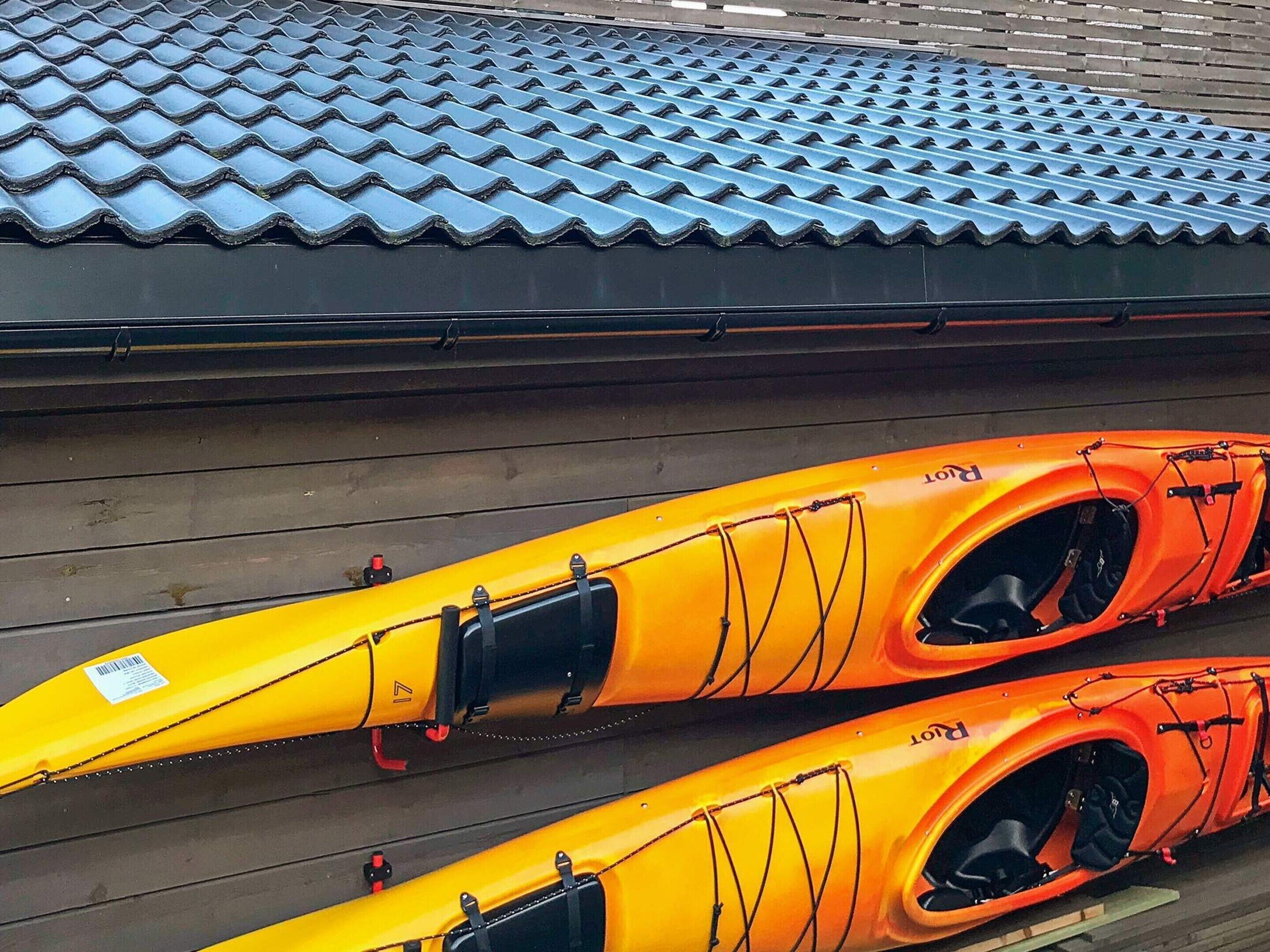 Deux kayaks jaunes ornés de détails noirs et de sangles de sécurité rouges, posés sur un plancher en bois, au-dessus duquel se trouve un toit recouvert de tuiles bleues.
