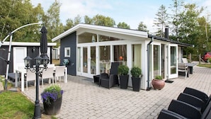Un espace extérieur moderne, aménagé en patio, avec un coin salon abrité, un barbecue et des plantes en pot.