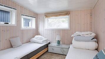 A bedroom with two single beds, a nightstand, a lamp, and a window with a curtain.