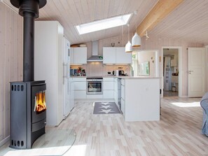 A modern kitchen with a wood-burning stove, white cabinetry, and pendant lighting. - 4 Star Holiday Home in Hojby (Hojby)