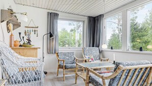 A cozy room with wicker furniture, a wooden table, and large windows offering a view of trees. - 6 Person Holiday Home in Saeby (Sæby)