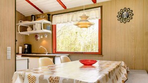 Uma cozinha compacta com uma janela, uma mesa de jantar com toalha de mesa estampada em formato de coração e uma tigela vermelha sobre a mesa.