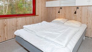 Quarto com uma grande janela, paredes de madeira, cama com roupa de cama branca e duas luminárias fixadas na parede.
