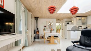 A modern living room with a TV, a fireplace, a dining area with a table and chairs, and a kitchen in the background. - 6 Person Holiday Home in Rodby (Rodby)