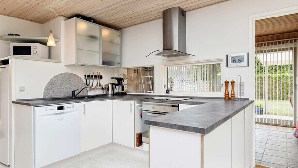 A modern kitchen with white cabinetry, a central island, and a built-in microwave. - 6 Person Holiday Home in Rodby (Rodby)