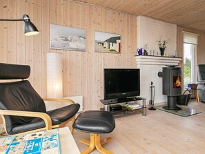Uma sala de estar aconchegante com televisão, paredes de madeira, lareira e um espaço de estar confortável.