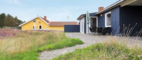 A residential property with a paved patio, outdoor seating, and a pathway leading to a yellow house.