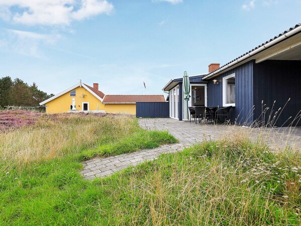 A residential property with a paved patio, outdoor seating, and a pathway leading to a yellow house.