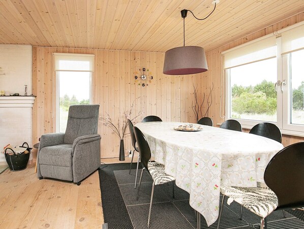 A dining area with a table set for four, surrounded by chairs, a grey armchair, and a hanging lamp.