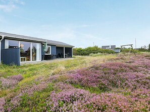 A modern house with a covered patio, a swing set, and a field of purple flowers.