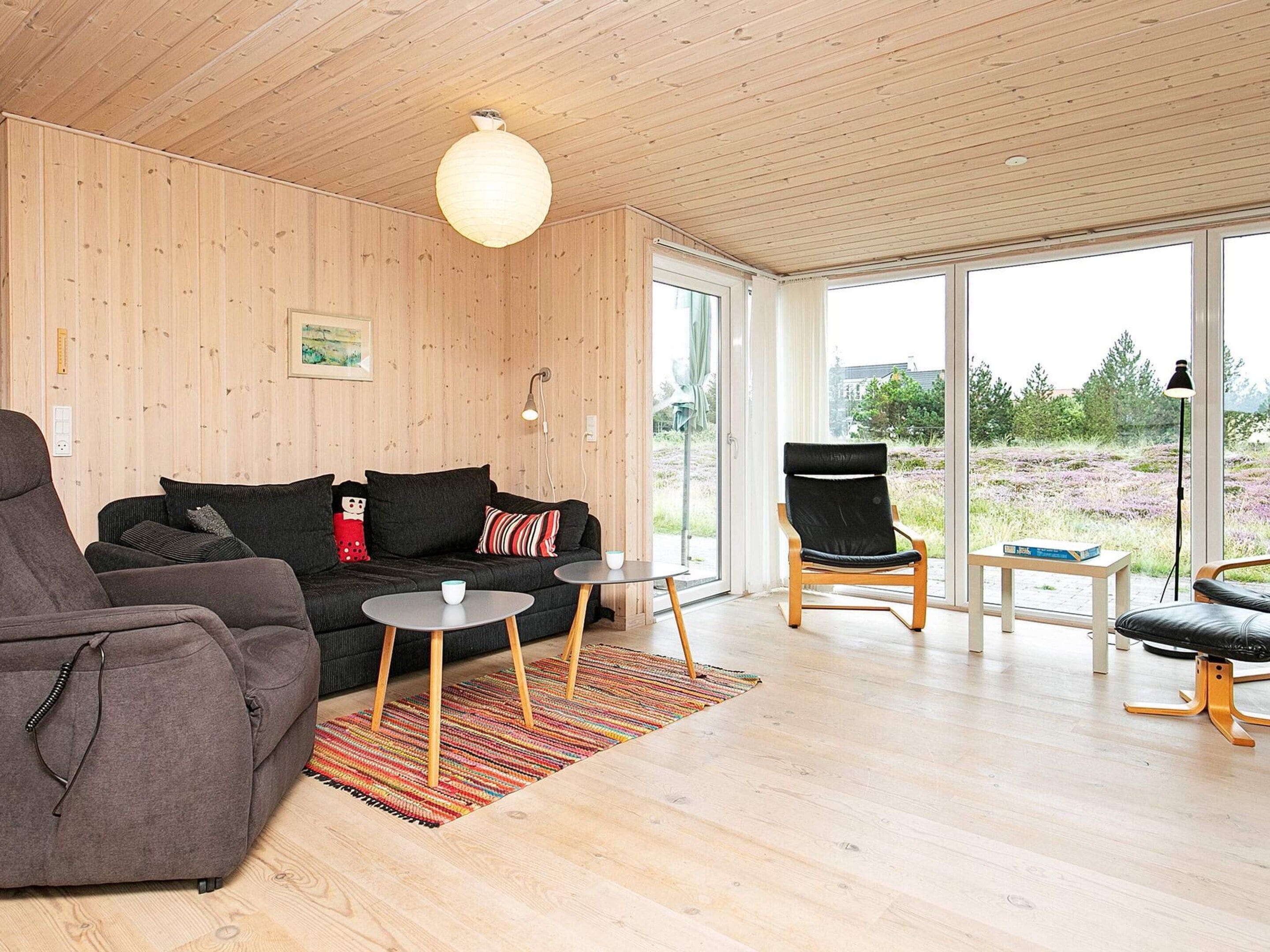 Ein modernes Wohnzimmer mit einer Couch, einem Sessel, einem Couchtisch und Blick durch große Fenster.
