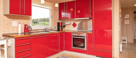 Una cocina con armarios rojos, un horno de acero inoxidable, una cafetera y un ventanal con vistas a zonas verdes.