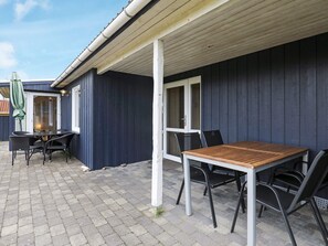 An outdoor patio area with a table and chairs, a covered seating area, and a building with dark siding.