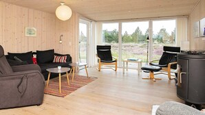 Un salon moderne avec un plafond en bois, de grandes fenêtres, un canapé, deux fauteuils, une petite table et une cheminée.