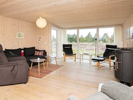 En moderne stue med træloft, store vinduer, en sofa, to stole, et lille bord og en pejs.