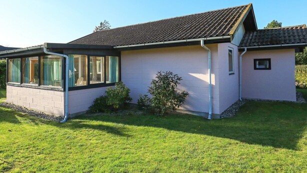 A single-story house with a tiled roof, a covered porch with glass doors, and a small garden area. - 4 Star Holiday Home in Vaeggerlose (Vaeggerlose)