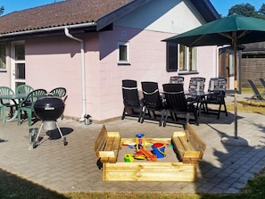 A patio with a grill, chairs, and a wooden play area. - 4 Star Holiday Home in Vaeggerlose (Vaeggerlose)