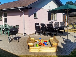 A patio with a grill, chairs, and a wooden play area. - 5 Person Holiday Home in Vaeggerlose (Vaeggerlose)